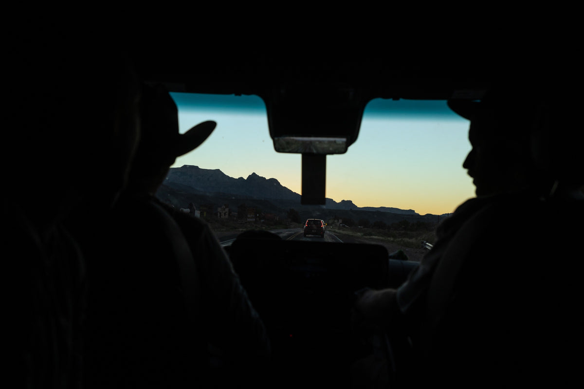 Silhouettes in a truck cab with the desert sunrise through the windshield. Photo: Robin O'Neill.