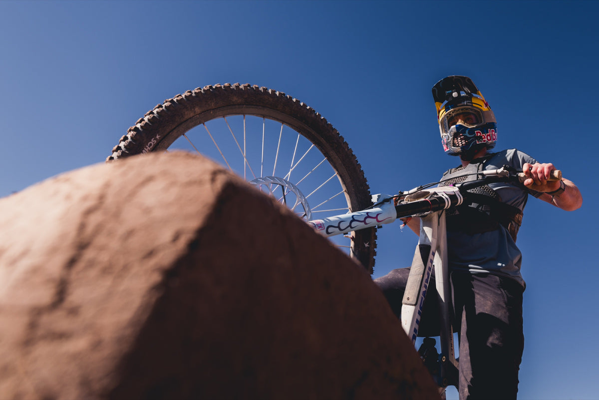 A rider in a full-face helmet lifts their bike over a sandstone lip. Photo: Robin O'Neill.