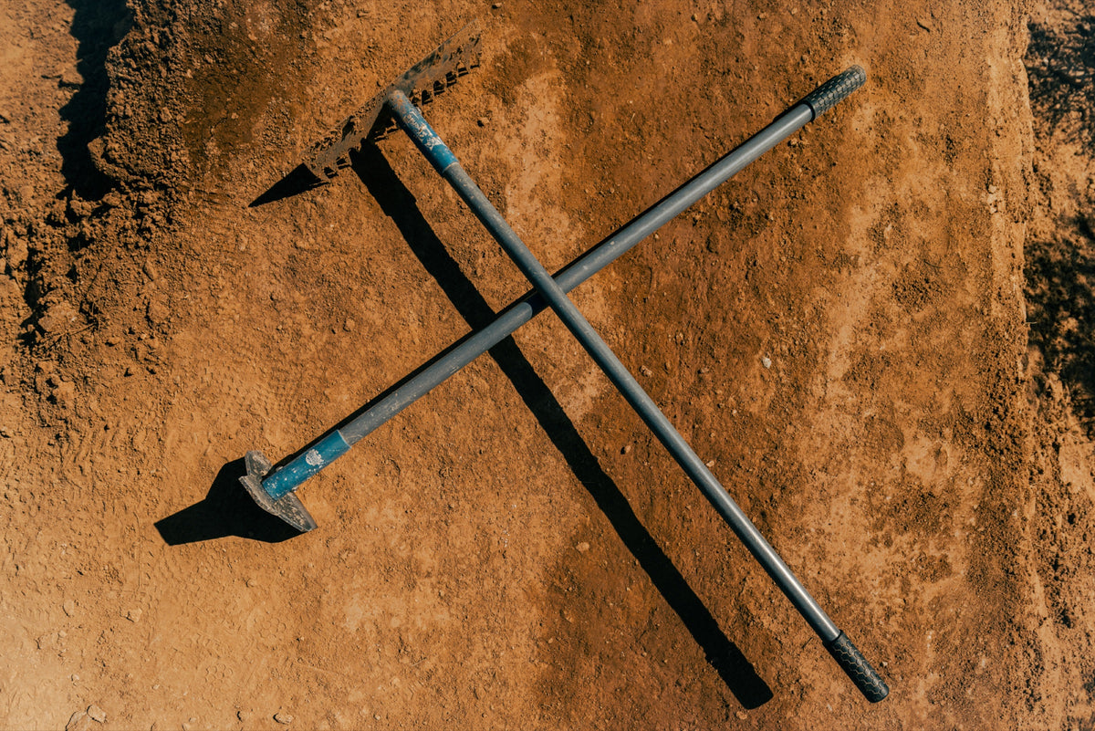 A shovel and a pick crossed on red dirt, seen from above. Photo: Robin O'Neill.