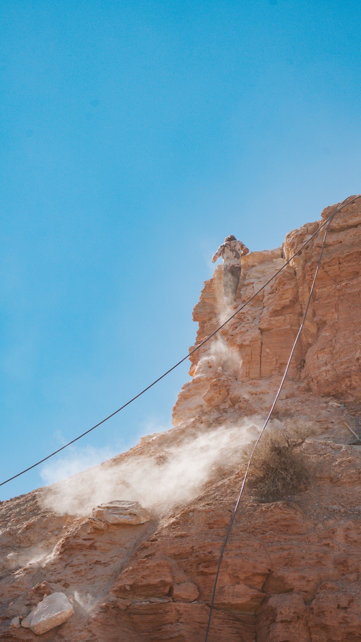 Dust rises off a cliff as a crew digs below the rim.